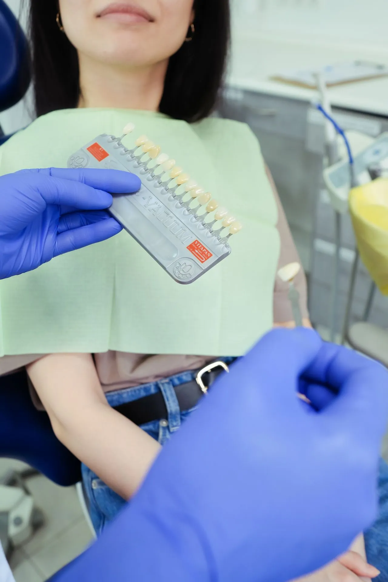 Dentist matching tooth shade with colour guide during cosmetic consultation — the personalised approach UK patients receive before veneers or Hollywood Smile treatment