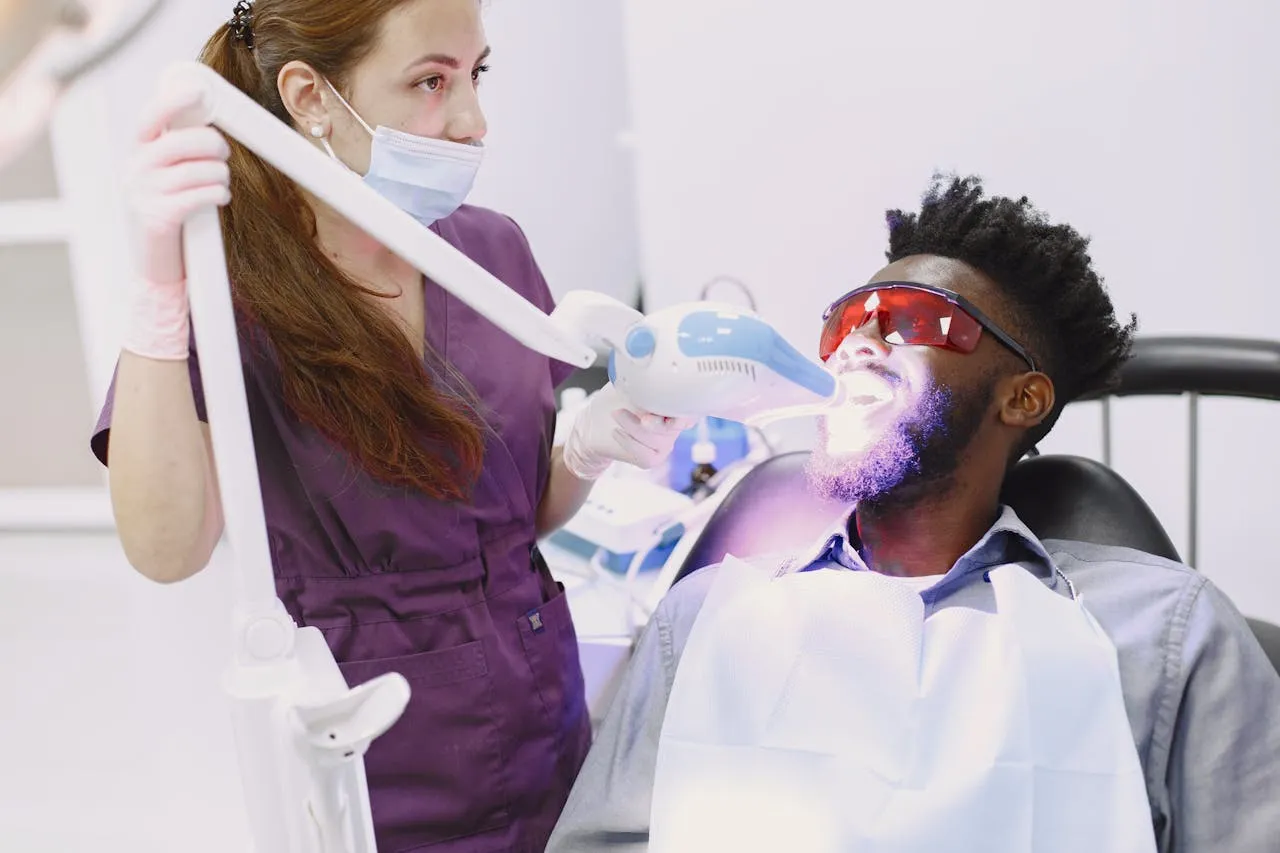 Dentist performing professional laser teeth whitening using UV activation light — patient wearing protective eyewear during in-office power bleaching session